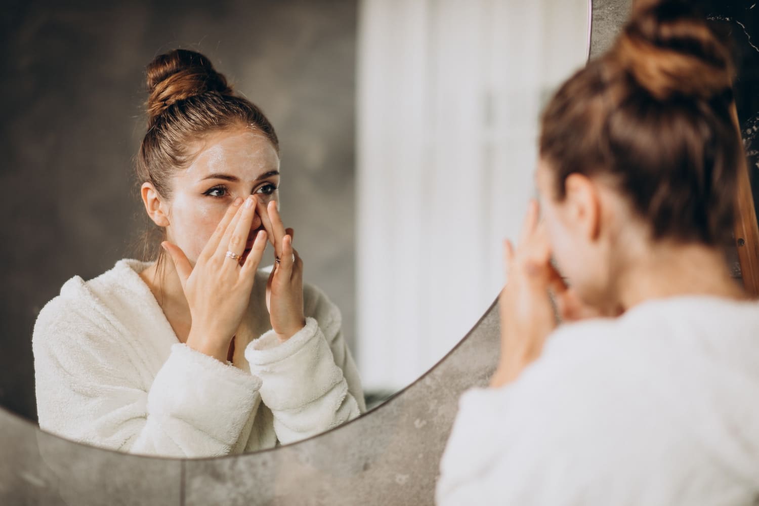 Imagem mulher passando creme no rosto na frente do espelho